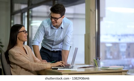 Happy businessman looking at pretty colleague in eyeglasses working on laptop - Shutterstock ID 1382908646