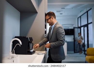 Happy businessman making himself u cup of coffee while working in the office. Copy space. - Powered by Shutterstock