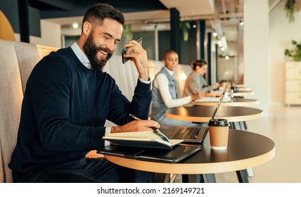 Happy businessman making notes during a phone call. Young businessman smiling cheerfully while making plans with his associates over the phone. Young entrepreneur working in a co-working space. - Shutterstock ID 2169149721