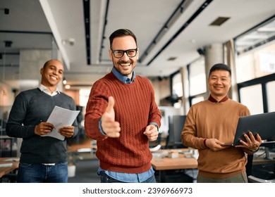 Happy businessman offering a handshake in front of his coworkers in the office and looking at camera. - Powered by Shutterstock