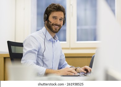 Happy Businessman In The Office On The Phone, Headset, Skype. Looking Camera