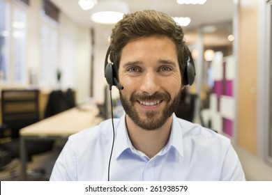 Happy Businessman in the office on the phone, headset, Skype. looking camera