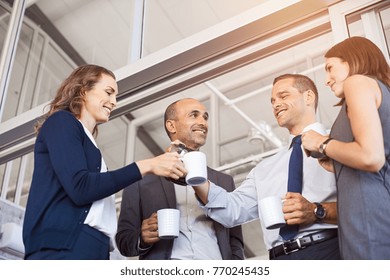 Happy businessman pouring coffee to his colleagues in meeting room. Smiling group of businessmen and businesswoman relaxing. Low angle view of formal business team take a coffe break after work. - Powered by Shutterstock