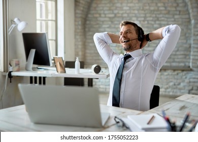 Happy businessman relaxing with hands behind head after working on laptop in the office. 