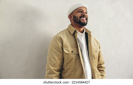 Happy businessman with a septum ring smiling while standing against a grey wall. Cheerful millennial businessman wearing business casual with jewellery in a modern office. - Powered by Shutterstock