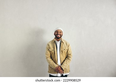 Happy businessman with a septum ring smiling at the camera while standing against a grey wall. Millennial businessman wearing business casual with jewellery in a modern workplace. - Powered by Shutterstock