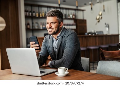 A happy businessman is sitting in a coffee shop and checking on his bank account on the mobile. There is a laptop on a table. A man using the phone for e-banking - Shutterstock ID 2078709274