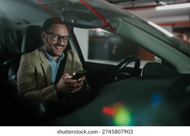 Happy businessman smiling while using smartphone in car, connecting and communicating online with technology