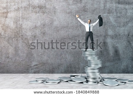 Happy businessman standing on silver coins on concrete wall background. Finance and success concept.