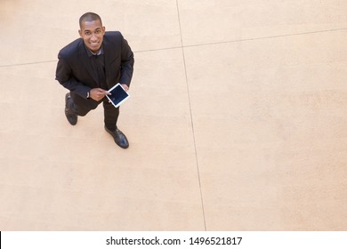 Happy Businessman With Tablet Walking Through Office Hall. Top View Of Young African American Business Man Holding Digital Device, Looking At Camera And Smiling. Top View Of Businessman Concept