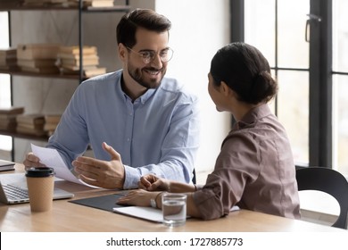 Happy businessman talking with indian businesswoman about successful finance report looking at worker. Diverse smiling woman and male manager discuss and looking decision in negotiation.