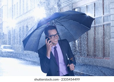 Happy businessman talking on cell phone under umbrella in rainy street - Powered by Shutterstock