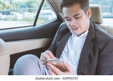 Happy Businessman Using Smartphone Calling While Driving The Car On His Morning Commute To Work. Handsome Asian Young Man Touching Mobile Phone Communication On His Luxury Automobile On The Road Trip.