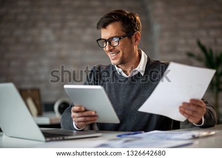 Happy businessman using touchpad and laptop while working on business reports in the office. 