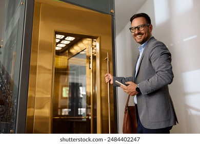 Happy businessman waiting for the elevator in a hallway and looking at camera. Copy space.  - Powered by Shutterstock