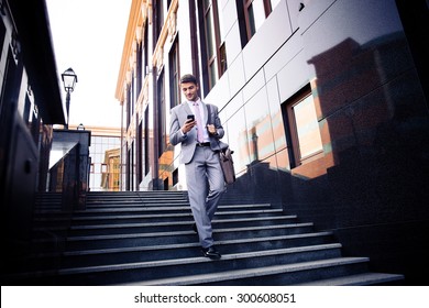 Happy Businessman Walking On The Stairs And Using Smartphone Outdoors