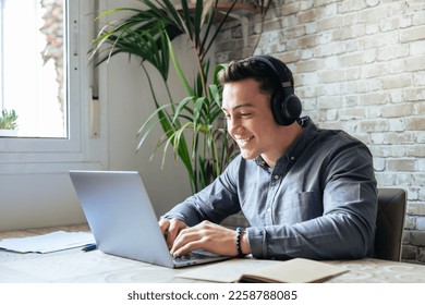 Happy businessman wearing headphones singing song at workplace, funny employee or freelancer using laptop, enjoying favorite track, listening to music, dancing, having fun during break - Powered by Shutterstock