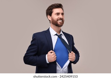 Happy businessman wearing superhero costume under suit on beige background