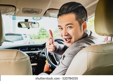 Happy Businessman While Driving Car And Smiling On His Morning Commute To Work. Asian Young Man On His Pointing Finger Forward On Automobile In The Road Trip. Copy Space