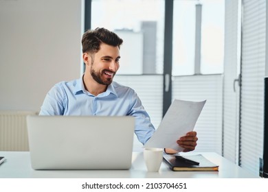 Happy businessman working by the desk looking on document - Shutterstock ID 2103704651