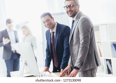 happy businessmen smiling at camera while leaning at table with desktop computer at workplace - Shutterstock ID 1273130098