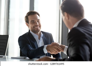 Happy businessmen in suits shaking hands after successful negotiations at meeting, male partners making business deal or good impression, thanking promising loyalty, respect gratitude handshake