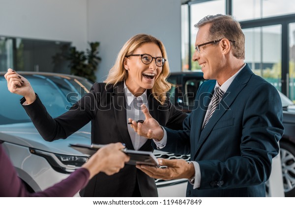 happy businesspeople and female car dealer with\
documents in showroom