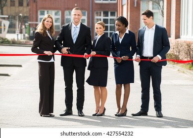 Happy Businesspeople At Opening Cutting Ribbon With Scissor