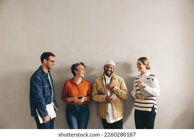 Happy businesspeople smiling cheerfully while waiting in line for an interview. Group of shortlisted job candidates holding different digital devices in a modern workplace. - Shutterstock ID 2260280187