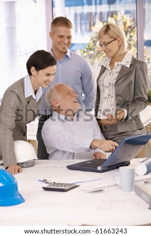 Happy businessteam busy at work, senior businessman pointing at laptop computer screen, laughing.?