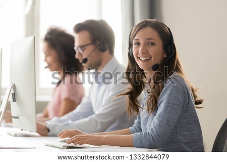 Happy businesswoman call center agent looking at camera posing at workplace, smiling female telemarketer operator in wireless headset working with computer in customer service support office portrait
