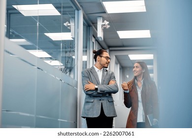 Happy businesswoman communicating with Hispanic male coworker while walking through hallway. Copy space.  - Powered by Shutterstock