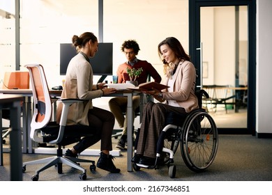 Happy businesswoman with disability and her female colleague cooperating while working on paperwork in the office. 