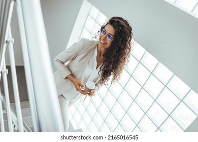 Happy Businesswoman With Frizzy Hair Looking Away Against Wall. Thoughtful Female Professional Is Holding Disposable Cup. She Is Wearing Suit