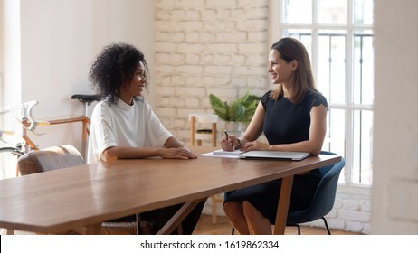 Happy businesswoman hr manager employer holding interview with applicant African American woman, talking, asking questions, good first impression, skilled job seeker at meeting in modern office