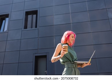 happy businesswoman with pink hair holding paper cup and using laptop outside - Powered by Shutterstock