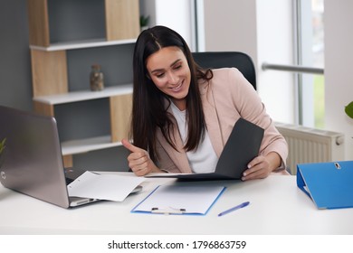 Happy Businesswoman With Raised So Hand Gesture Reading Letter On Desk In Front Of Laptop. The Businessman Is Satisfied With The Good News From The Correspondence.