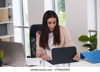 Happy Businesswoman With Raised So Hand Gesture Reading Letter On Desk In Front Of Laptop. The Businessman Is Satisfied With The Good News From The Correspondence.