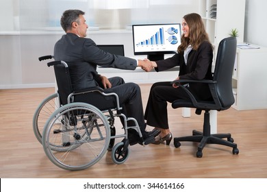 Happy Businesswoman Shaking Hands With Disabled Businessman In Office