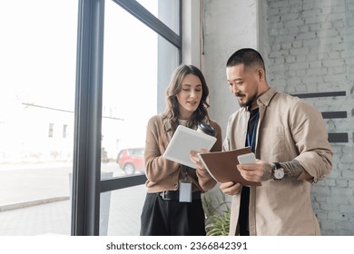 happy businesswoman showing tablet with startup project to asian colleague in modern office - Powered by Shutterstock