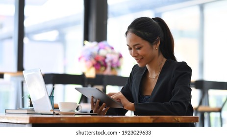 Happy businesswoman sitting in front of computer laptop and using digital tablet.