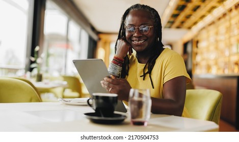 Happy businesswoman smiling at the camera while holding a digital tablet in a cafe. Self-employed senior woman doing some online freelance work in a coffee shop. - Powered by Shutterstock