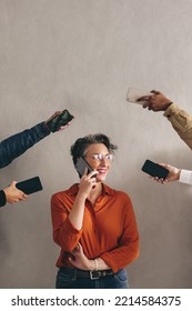 Happy Businesswoman Speaking On The Phone While Surrounded By Hands Holding Smartphones. Cheerful Businesswoman Smiling While Answering Phone Calls In A Busy Work Environment.