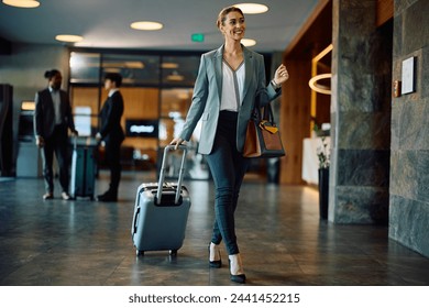 Happy businesswoman with suitcase walking through hotel lobby. Copy space.  - Powered by Shutterstock