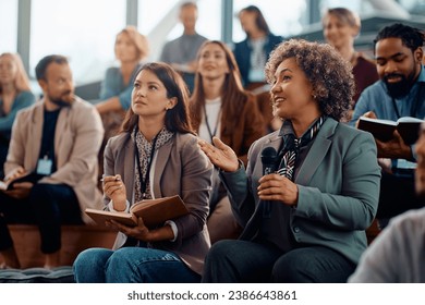 Happy businesswoman talking on microphone while attending education event in conference hall. - Powered by Shutterstock