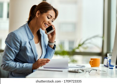 Happy businesswoman talking on mobile phone while analyzing weekly schedule in her notebook.