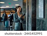 Happy businesswoman texting on mobile phone while waiting for elevator in a hotel. Copy space.