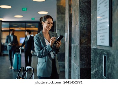 Happy businesswoman texting on mobile phone while waiting for elevator in a hotel. Copy space. - Powered by Shutterstock
