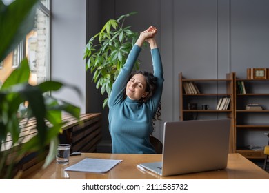 Happy businesswoman warming up body and muscles at workplace, feeling satisfied with work done, smiling female employee resting from computer screen. Well-being, productivity and happiness at work - Shutterstock ID 2111585732