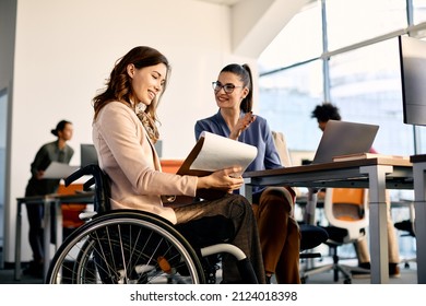 Happy businesswoman in wheelchair going through reports while talking to female coworker in the office. - Powered by Shutterstock